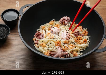 Mescolare gli spaghetti fritti con i frutti di mare nel wok sul tavolo di legno Foto Stock