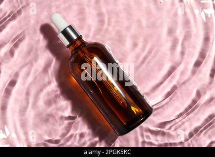 Bottiglia di olio idrofilo in acqua su sfondo rosa, vista dall'alto. Spazio per il testo Foto Stock