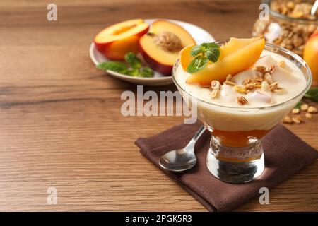 Gustoso yogurt alla pesca con muesli, menta e frutta in ciotola da dessert su tavolo di legno, spazio per testo Foto Stock