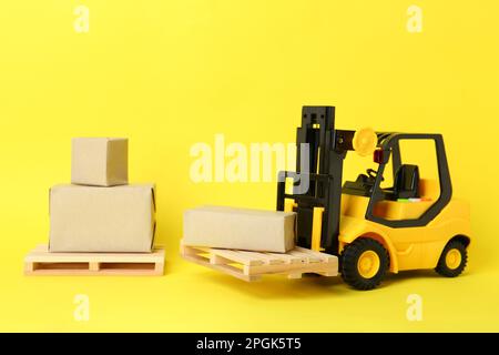 Carrello giocattolo, pallet in legno e scatole su sfondo giallo Foto Stock