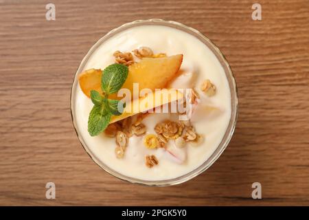 Gustoso yogurt alla pesca con muesli, menta e frutta in ciotola da dessert su tavolo in legno, vista dall'alto Foto Stock