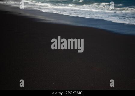 La maggior parte delle spiagge di sabbia nera sfocata con la schiuma bianca delle onde del mare Foto Stock