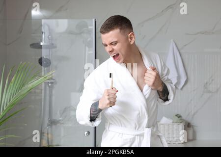 Bel giovane uomo che canta nello spazzolino da denti in bagno Foto Stock