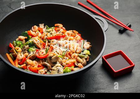 Mescolare le tagliatelle fritte con funghi, gamberetti e verdure in wok sul tavolo nero, primo piano Foto Stock
