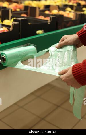 Uomo che prende il sacchetto di plastica dal supporto vicino alle casse con frutta nel supermercato, primo piano Foto Stock