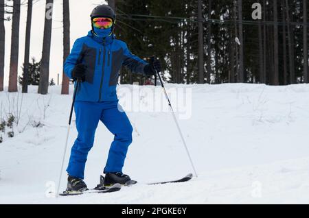 Un uomo con abbigliamento sportivo blu sugli sci si trova sullo sfondo di una pista innevata Foto Stock