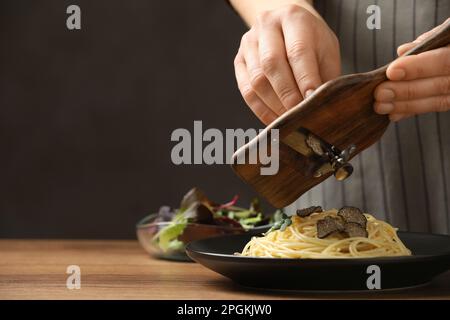 Donna affettare il tartufo su spaghetti a tavola di legno, primo piano Foto Stock