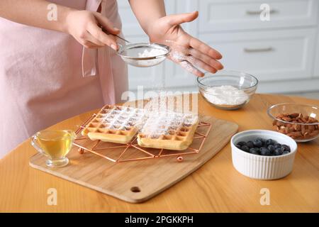 Donna decorazione deliziosi waffle belgi con zucchero a velo al tavolo in legno in cucina, primo piano Foto Stock