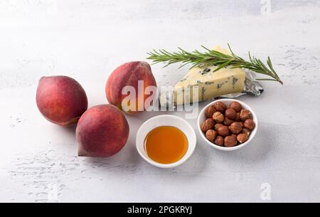 Ingredienti per pesche al forno: Pesche fresche, formaggio azzurro, nocciole, miele e rosmarino su sfondo grigio chiaro, vista dall'alto Foto Stock