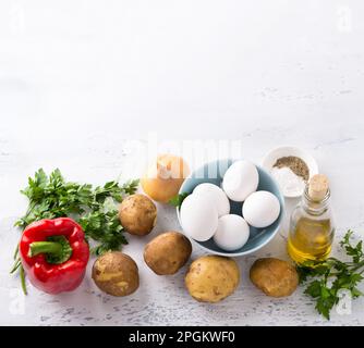 Ingredienti per tortilla o omelette spagnola - patate giovani, peperoni, cipolle, prezzemolo, olio d'oliva e spezie su sfondo grigio chiaro, vista dall'alto, Foto Stock
