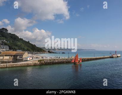 Il molo Banjo a East Looe in Cornovaglia. Navigando lungo il fiume, un lugro rosso da pesca a vela. Foto Stock