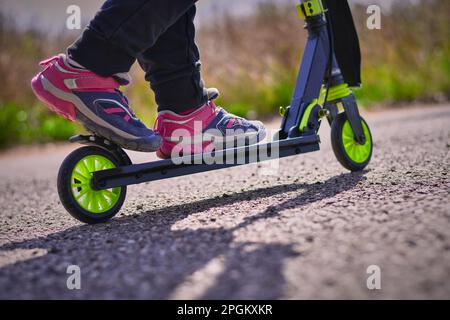 Una ragazza guida e frena con il piede la ruota posteriore di uno scooter su un rollerdrome con un asfalto. Foto Stock