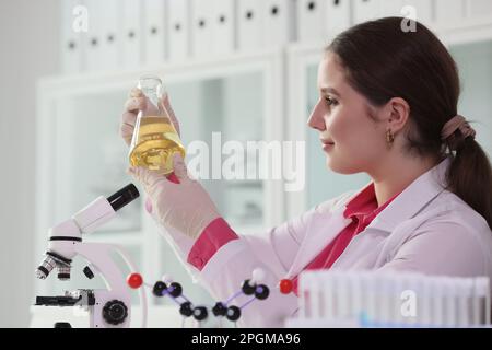 La donna Brunette tiene il pallone con olio giallo in laboratorio Foto Stock