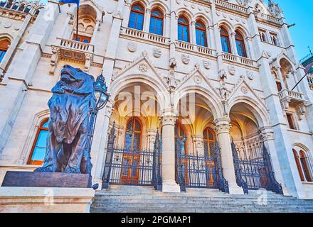 La statua del leone guardiano di fronte alla facciata del Parlamento ungherese, decorata in stile neogotico, Budapest, Ungheria Foto Stock