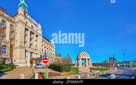 Panorama con la splendida Source House in pietra su Piazza Gellert con Gellert Hotel e il Ponte della libertà sullo sfondo, Budapest, Ungheria Foto Stock