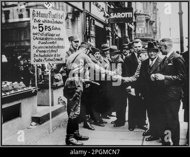 Germania nazista 1930s antisemitismo antisemitismo razzista ebreo SA pickets distribuire boicottaggio opuscoli ai pedoni tedeschi. Il segno tenuto da un membro di SA Sturmabteilung recita: "Attenzione tedeschi. Questi proprietari ebrei di [cinque e dime] negozi sono i parassiti e cimitatori di artigiani tedeschi. Pagano salari da fame ai lavoratori tedeschi. Il proprietario del negozio è l'ebreo, Nathan Schmidt." Antisemitismo nella Germania nazista Foto Stock