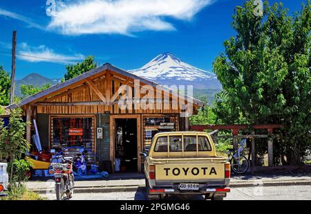 Conguillio NP, Cile: Dicembre 23. Giorno 2011: Tradizionale edificio del negozio di legno delle ande cilene, parcheggio per camion Toyota, vetta del vulcano llaima Foto Stock