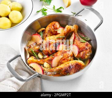 Bastoncini di pollo cotti con mele ed erbe in pentola su fondo bianco. Vista ravvicinata Foto Stock