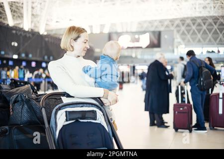 Motherat che viaggia con il suo bambino bambino, camminando, spingendo passeggino e carrello bagagli alla stazione terminale dell'aeroporto. Viaggiare con bambino con Foto Stock