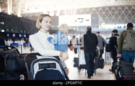 Motherat che viaggia con il suo bambino bambino, camminando, spingendo passeggino e carrello bagagli alla stazione terminale dell'aeroporto. Viaggiare con bambino con Foto Stock