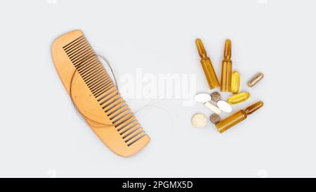 Ampolle cosmetiche con siero e vitamine per la crescita dei capelli, ripristino bellezza capelli. Pettine di legno con perdita di capelli su sfondo grigio. Perdita di capelli, baldne Foto Stock