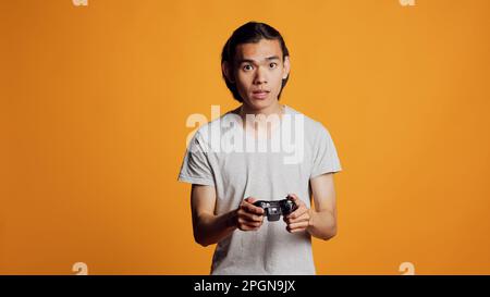 Moderno uomo asiatico che gioca a videogiochi su console, utilizzando il controller o il joystick per divertirsi con la concorrenza di gioco online. Giovane persona allegra che si diverti a sfidare su internet, giocare. Foto Stock