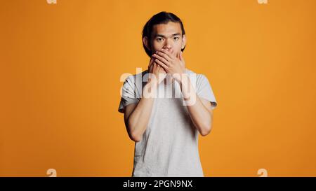 Ragazzo fiducioso hipster facendo tre scimmie saggio segno sulla fotocamera, utilizzando il linguaggio del corpo. Moderno e spensierato adulto che esprime non guardare, non parlare e non sentire il gesto in studio. Foto Stock