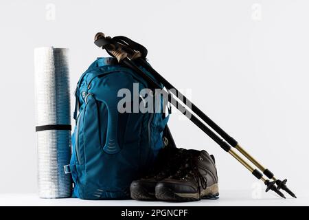 Primo piano di zaino blu, tappetino, scarpe da trekking e bastoni su sfondo bianco con spazio copia Foto Stock