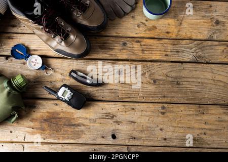 Attrezzatura da campeggio di scarpe da trekking, coppa di metallo e bussola su fondo in legno con spazio copia Foto Stock