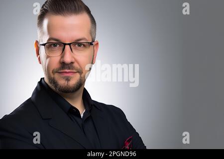 Un uomo che indossa occhiali e una camicia nera si pone per la fotocamera sorridendo con sicurezza Foto Stock