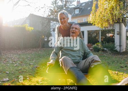 Felice coppia senior divertendosi con la carriola in giardino Foto Stock