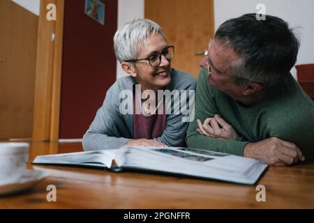 Felice coppia senior sdraiato sul pavimento a casa con album di foto Foto Stock