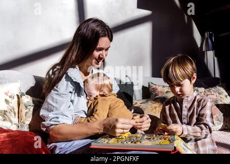 Madre sorridente che risolve puzzle con bambini a casa Foto Stock