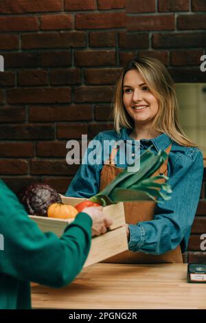 Sorridente proprietario che riceve cassa di verdure dalla persona di consegna al caffè Foto Stock