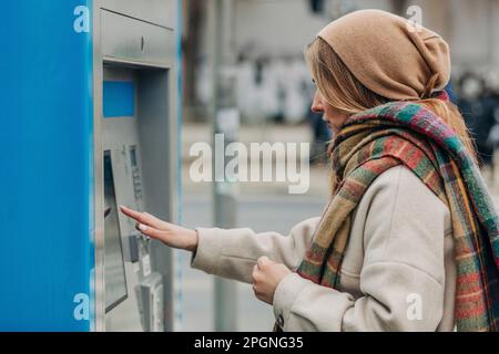 Giovane donna che usa il distributore automatico di biglietti Foto Stock