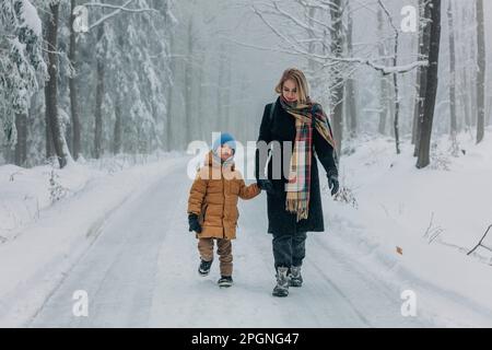 Madre che cammina con il figlio su strada nella foresta innevata Foto Stock