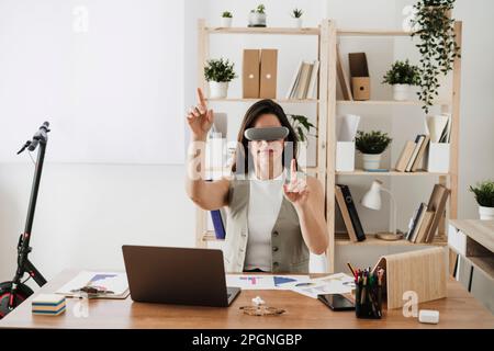 Donna d'affari che indossa occhiali VR seduti alla scrivania in ufficio Foto Stock