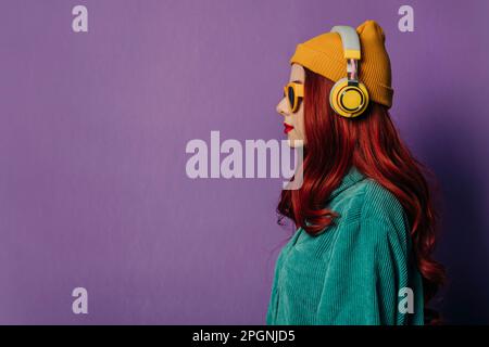 Donna rossa che ascolta la musica attraverso le cuffie su sfondo viola Foto Stock