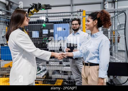 Donne d'affari che scuotono le mani da un uomo d'affari in fabbrica Foto Stock