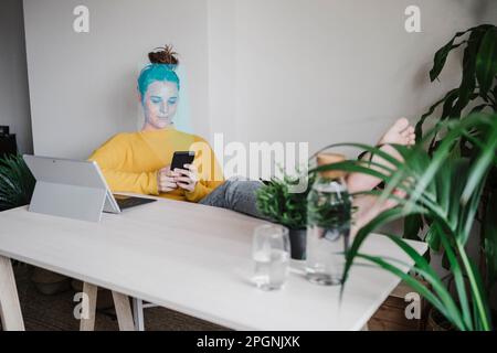 Freelance che utilizza lo smartphone seduto in ufficio Foto Stock
