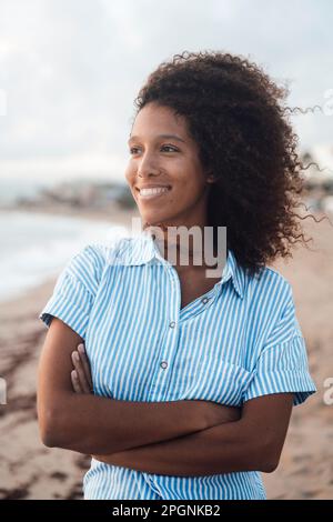 Donna felice con le braccia incrociate in piedi sulla costa in spiaggia Foto Stock