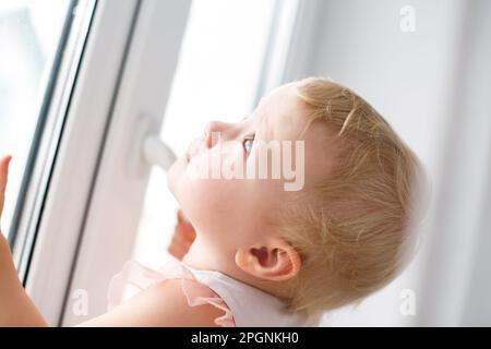 Un bambino di 3 anni in una T-shirt a righe apre una finestra