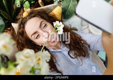 Donna che prende selfie con fiore sulle labbra puckering Foto Stock