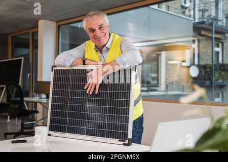 Ingegnere sorridente con pannello solare in ufficio Foto Stock