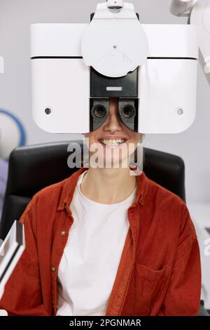 Paziente sorridente che fa il controllo dell'occhio in su attraverso il foropter alla clinica Foto Stock