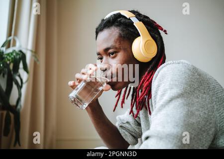 Giovane uomo attento che indossa cuffie con acqua potabile a casa Foto Stock