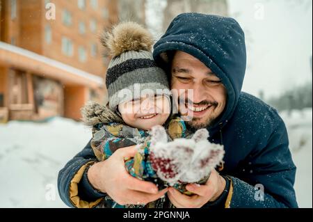 Padre e figlio indossano abiti caldi godendosi insieme nella neve Foto Stock
