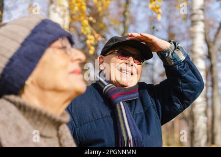 Uomo anziano sorridente che regola il cappello da donna al parco Foto Stock