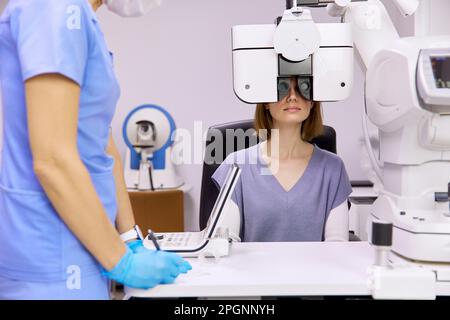 Il medico con il paziente che fa il controllo della vista attraverso il foropter alla clinica Foto Stock