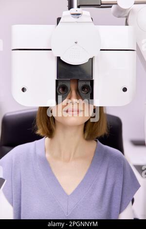 Paziente che esegue il controllo visivo attraverso il foropter presso la clinica Foto Stock